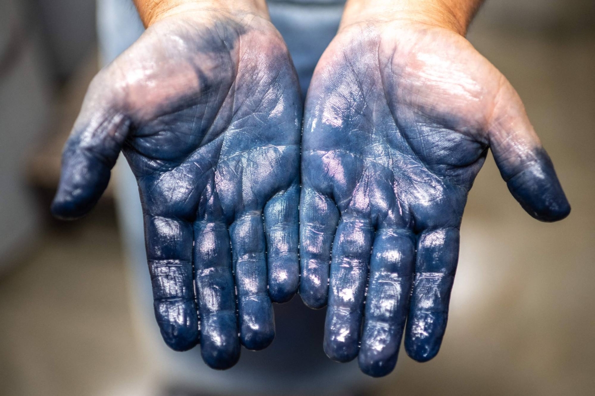 Cette photo, prise le 4 septembre 2024, montre les mains de l'artisan teinturier Yoshiharu Okamoto à l'usine Momotaro Jeans dans la ville de Kurashiki, dans le quartier de Kojima, préféfecture d'Okayama. Véritable antidote à la mode rapide : des jeans japonais teints à la main avec de l'indigo naturel et tissés sur d'anciens métiers à tisser.